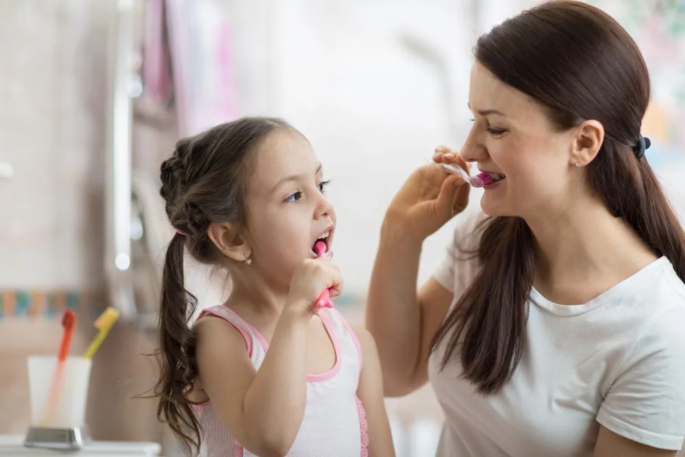Mother teaching her daughter to brush her teeth in the bathroom — dental clinic in Buderim, QLD